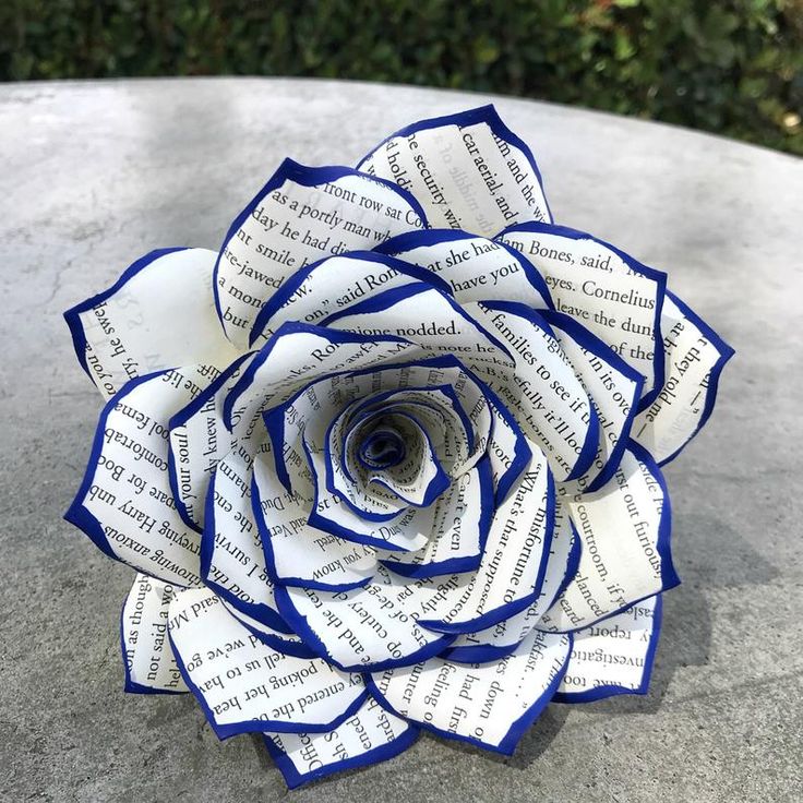 a blue and white paper rose sitting on top of a cement table next to bushes