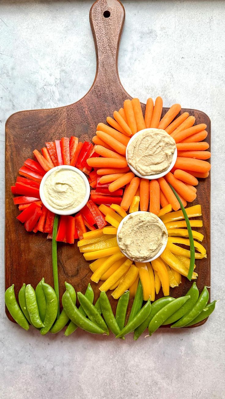 a cutting board with carrots, celery, peppers and dip on it