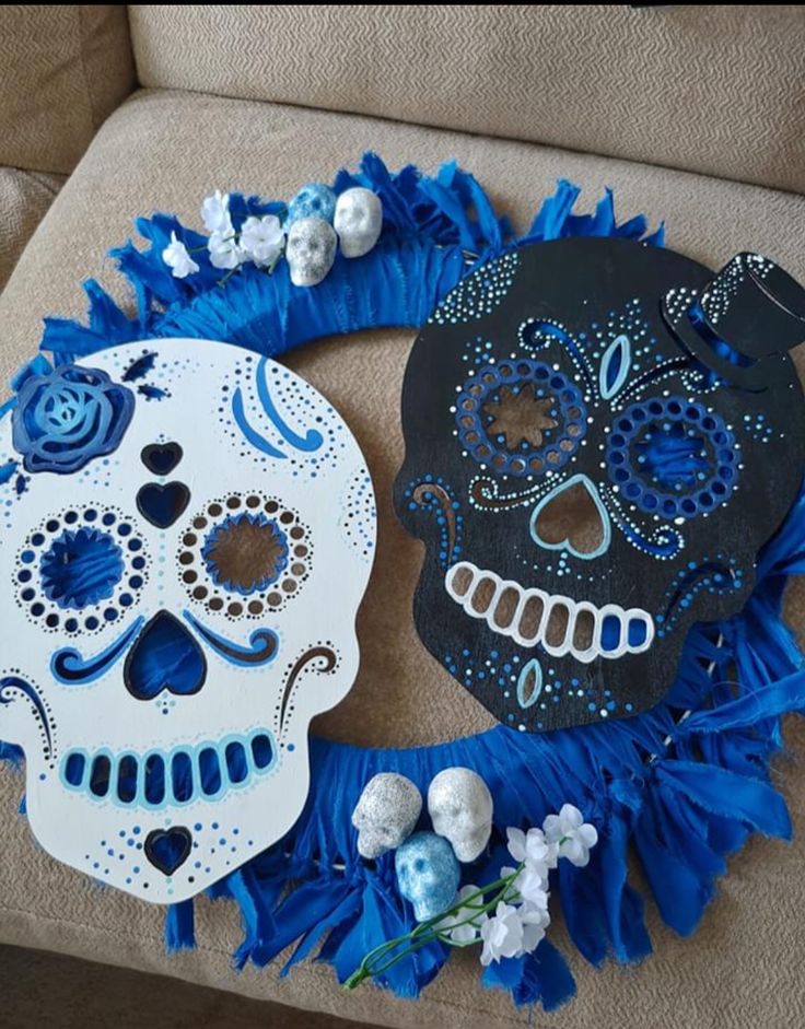 two sugar skulls decorated with blue and white flowers on a couch next to a decorative wreath