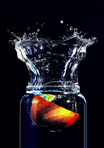 an apple in a glass jar with water splashing on it