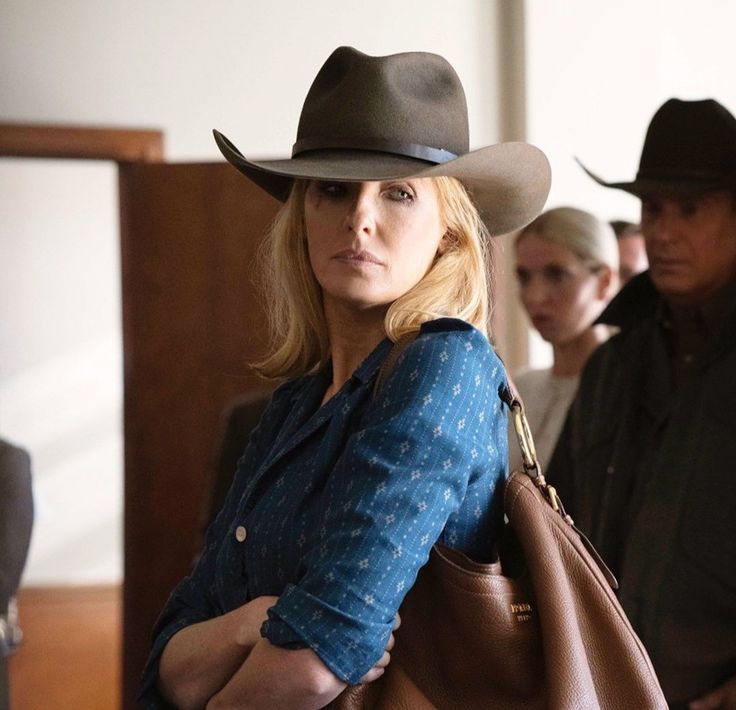 a woman wearing a cowboy hat and carrying a brown bag while standing next to other people