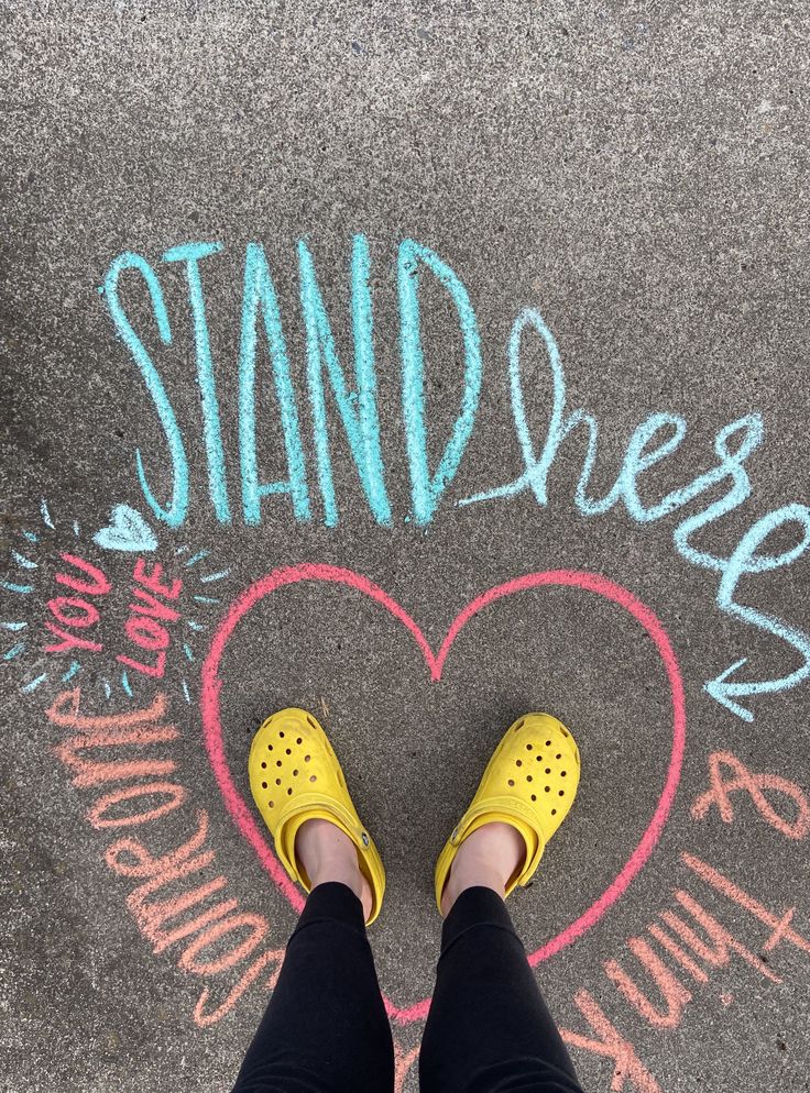 someone wearing yellow shoes standing in front of a chalk drawing that says stand up and love