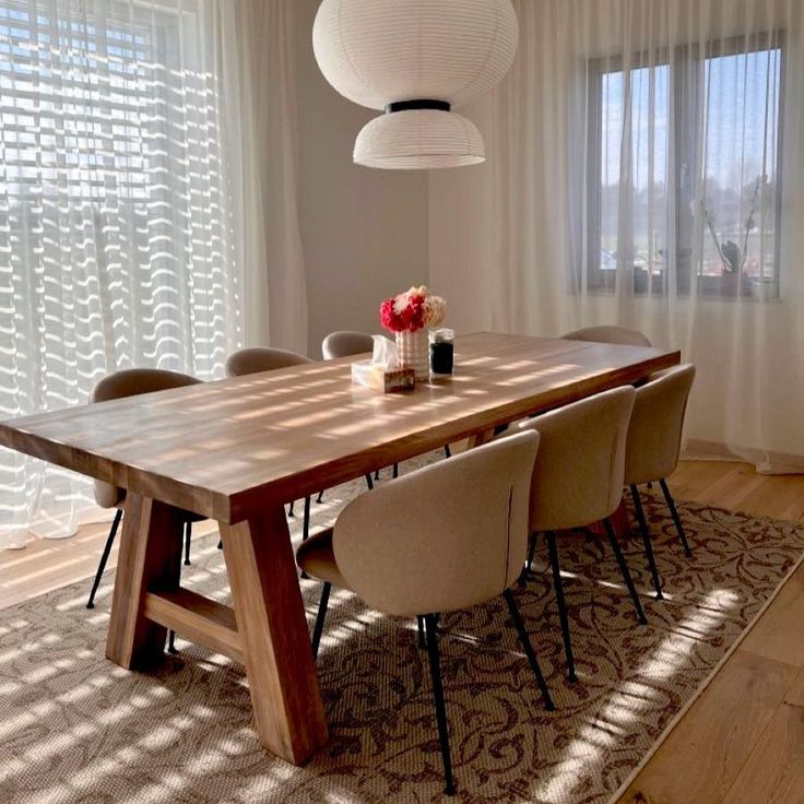 a dining room table and chairs in front of a window with sheered drapes