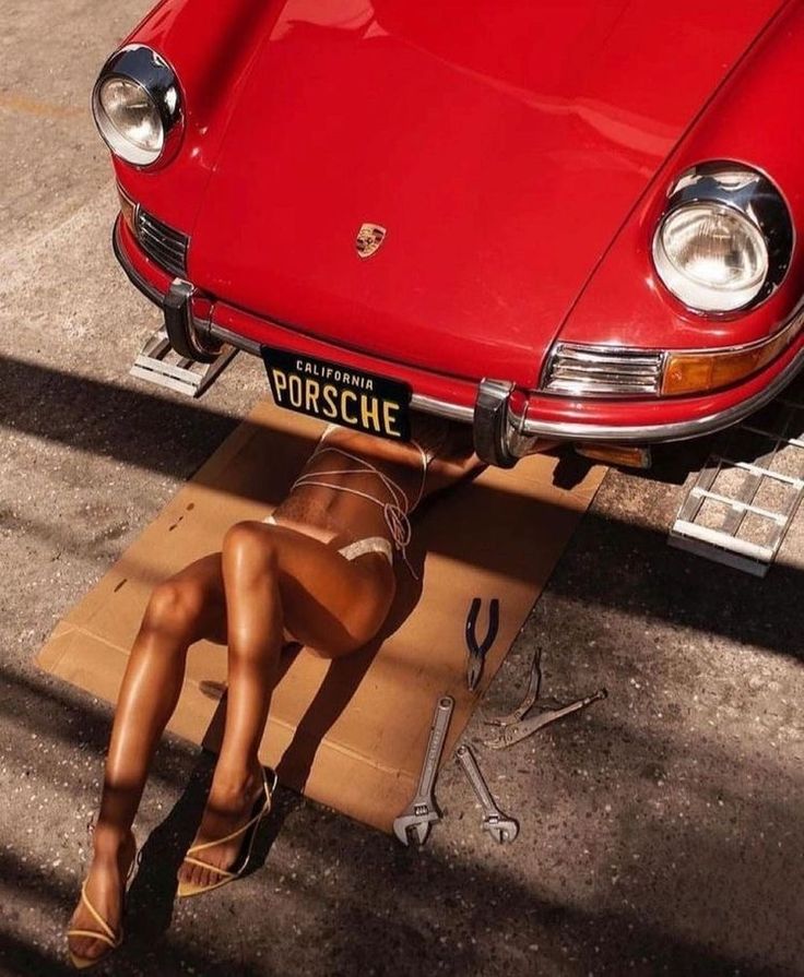 a woman laying on top of a cardboard box next to a red car with the license plate porsche