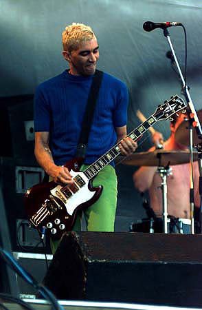 a man with blonde hair playing guitar on stage at a music festival in front of microphones