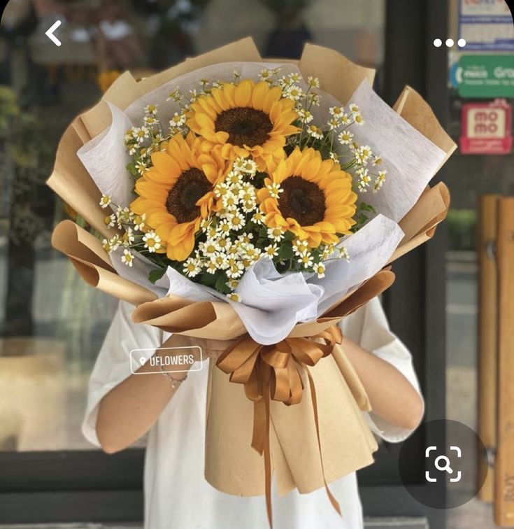 a woman holding a bouquet of sunflowers in front of a storefront window