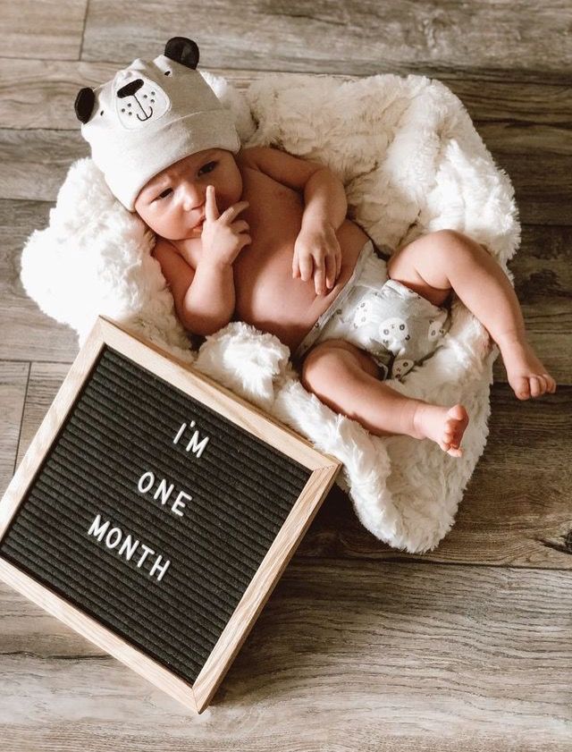 a baby laying on top of a white blanket next to a sign that says i'm one month