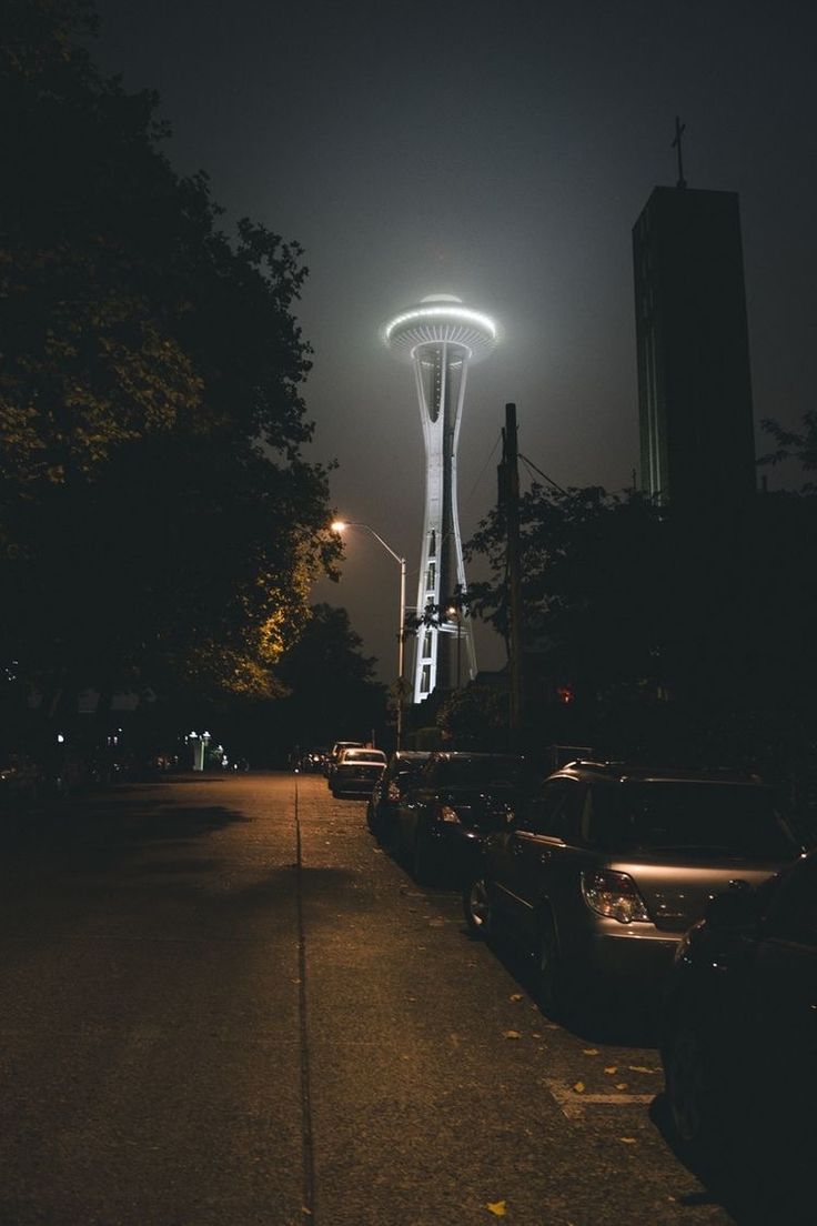 the space needle at night with cars parked on the street and lights in the background