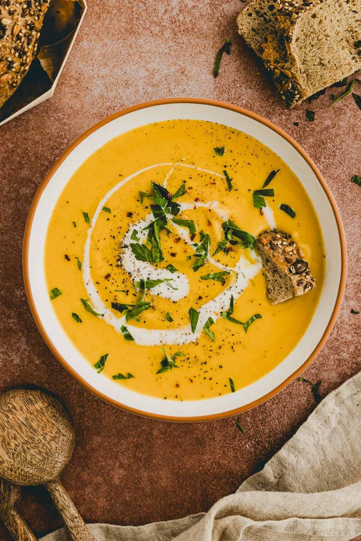 a white bowl filled with yellow soup and topped with sour cream, parmesan cheese and herbs