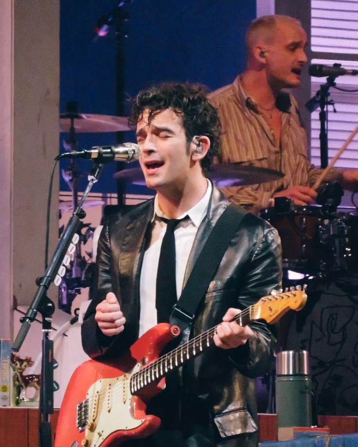 a man in a suit and tie playing an electric guitar while singing into a microphone