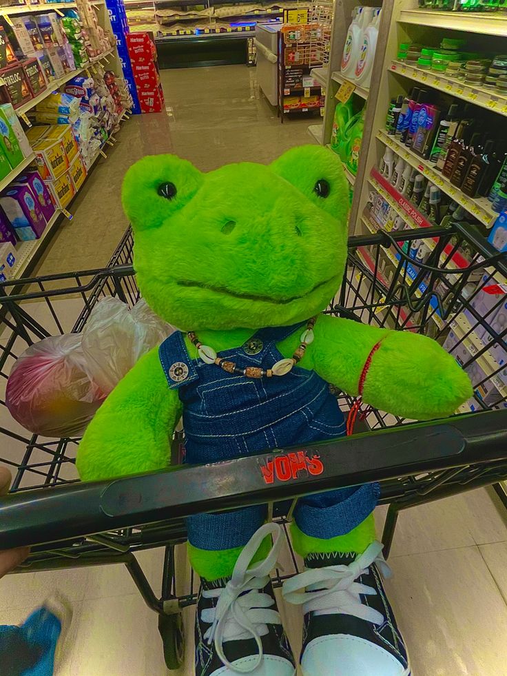 a green stuffed frog sitting in a shopping cart