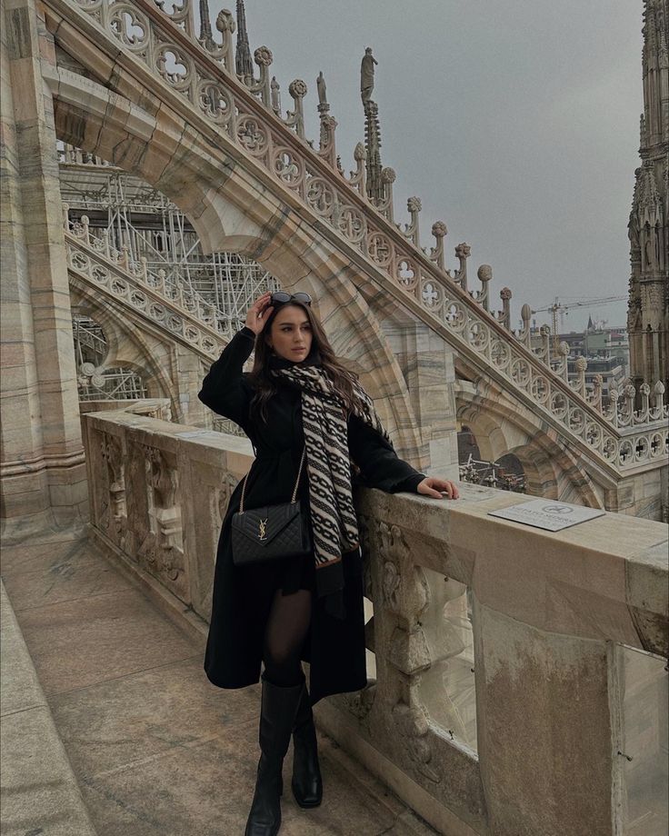 a woman standing on top of a bridge next to a tall building with ornate architecture