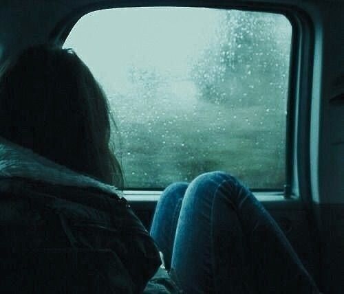 a woman sitting in the back seat of a car looking out a window at rain