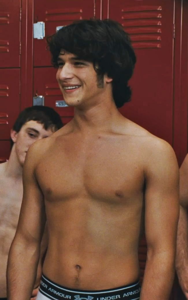 a shirtless young man standing in front of lockers