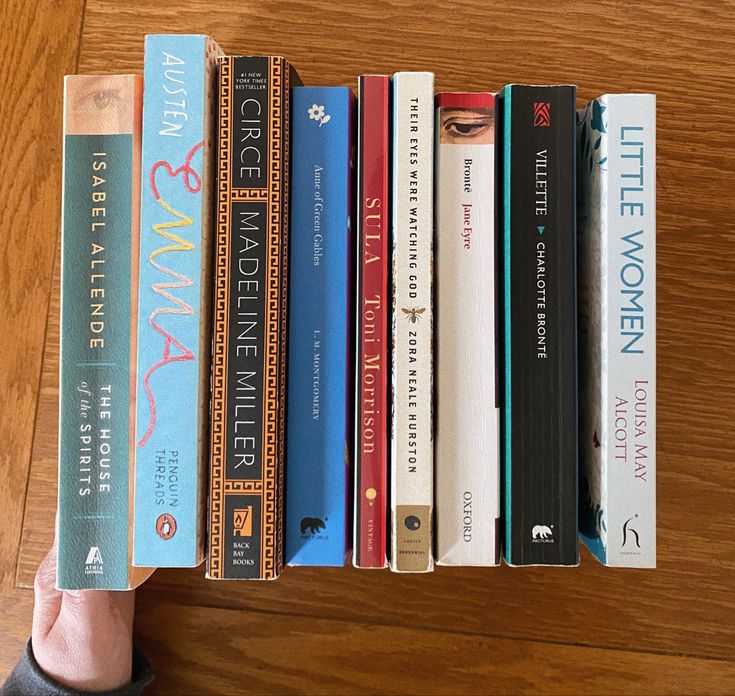 a person holding a book in front of a row of books on a wooden table