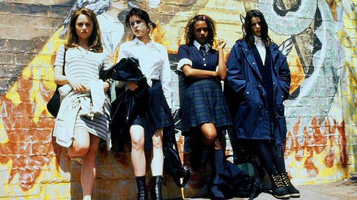 four girls in school uniforms are standing against a wall