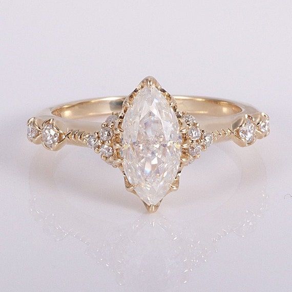 a white diamond ring with gold band and diamonds on the sides, sitting on a white surface