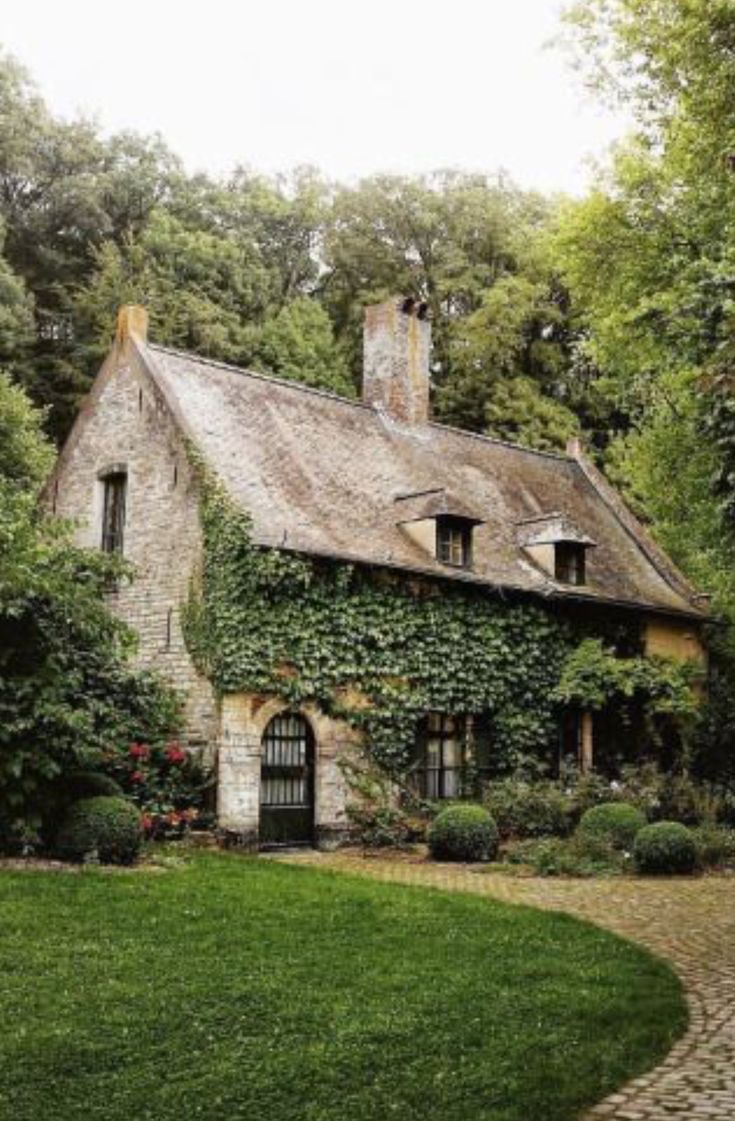 an old stone house with ivy growing on it's roof and windows, surrounded by greenery