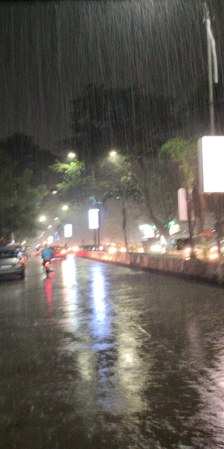 cars driving down the street in the rain at night with lights on and one person holding an umbrella