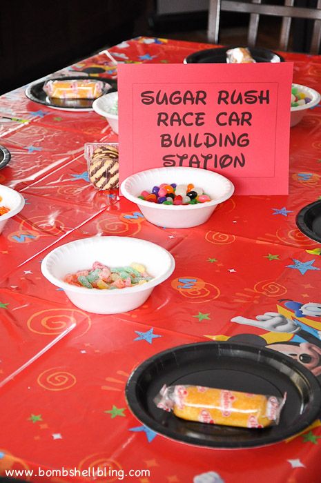 a red table topped with plates and bowls filled with food next to a sign that says sugar rush race car building station