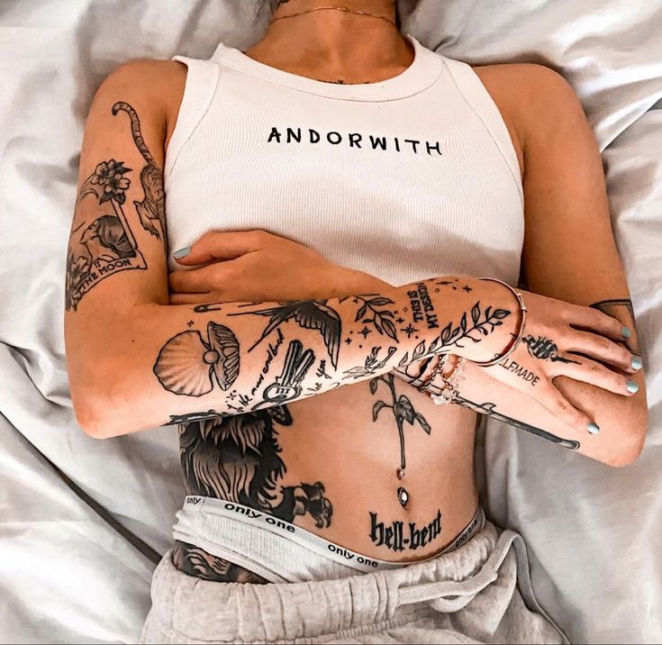 a woman laying in bed with tattoos on her stomach and arms behind her head is a white tank top