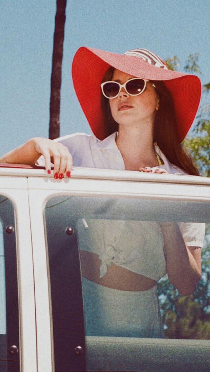 a woman wearing a red hat and sunglasses sitting in the back of a white truck