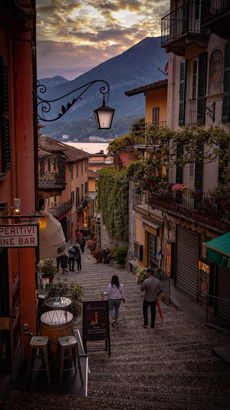 people are walking down an alley way with umbrellas on the side and mountains in the background