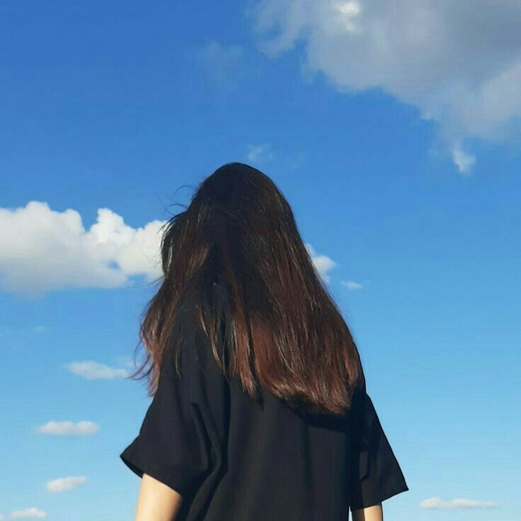 a woman with long hair standing in front of a blue sky looking up at the clouds