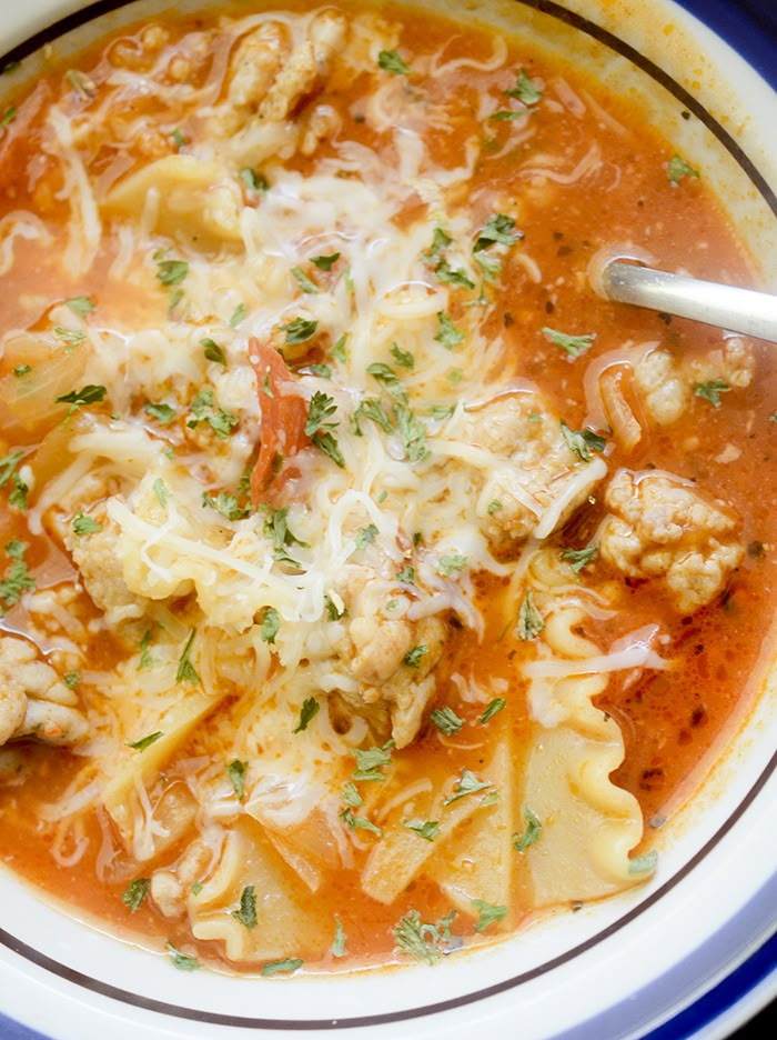 a bowl of soup with meat, noodles and parmesan cheese on top is shown