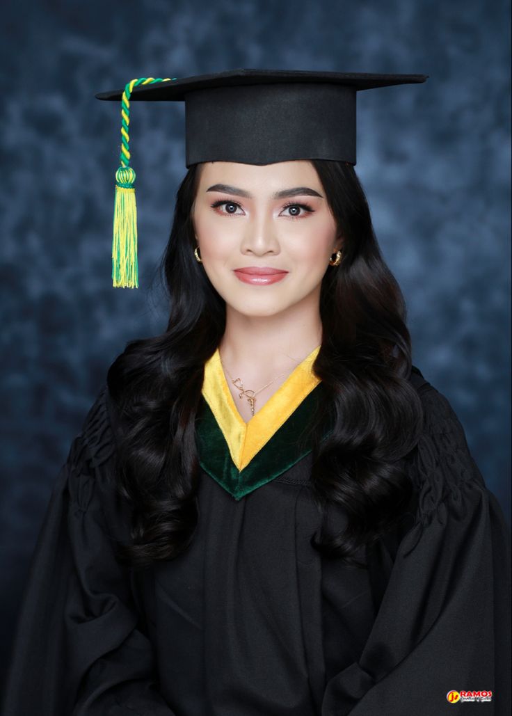 a woman wearing a graduation cap and gown in front of a blue background with a green tassel