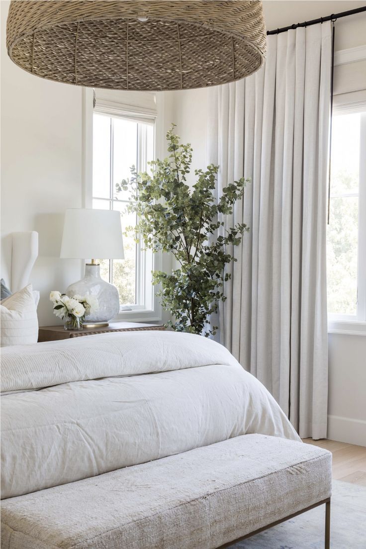 a bed with white linens and pillows in a bedroom next to a plant on a table