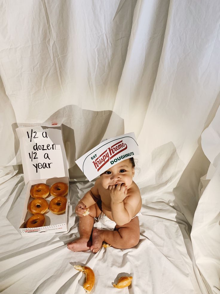 a baby wearing a krispy kreme hat next to a box of doughnuts