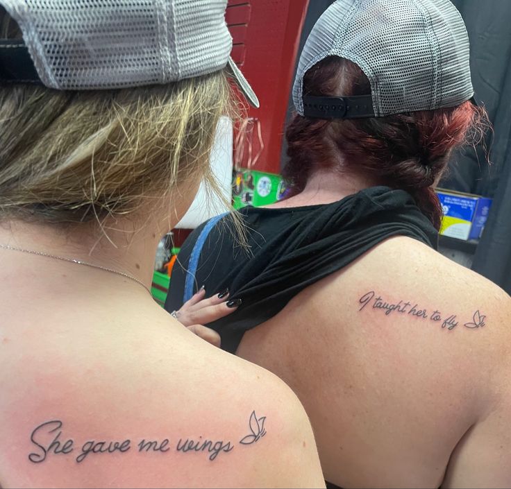 two women with tattoos on their backs looking at each other and the words are written in cursive writing