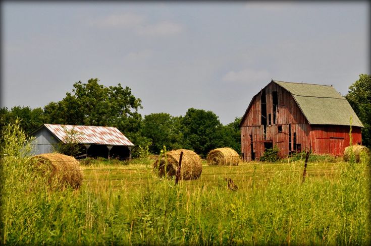 an old barn and hay bails in a field