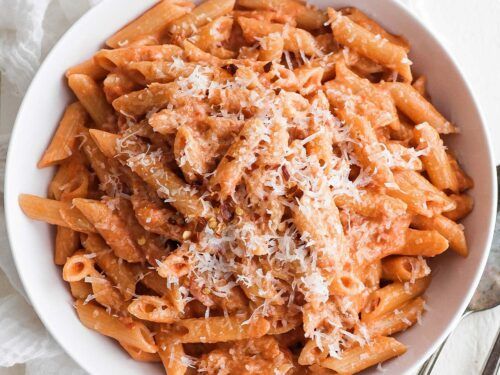 a white bowl filled with pasta covered in sauce and parmesan cheese