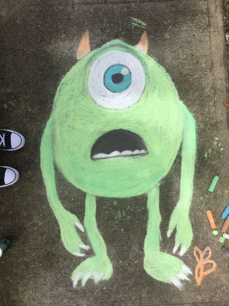 a drawing of a green monster with big eyes on the ground next to some crayons