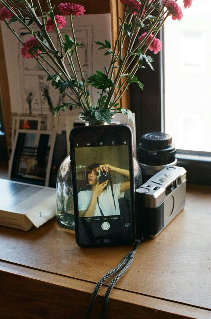 a cell phone sitting on top of a wooden table next to a vase filled with flowers