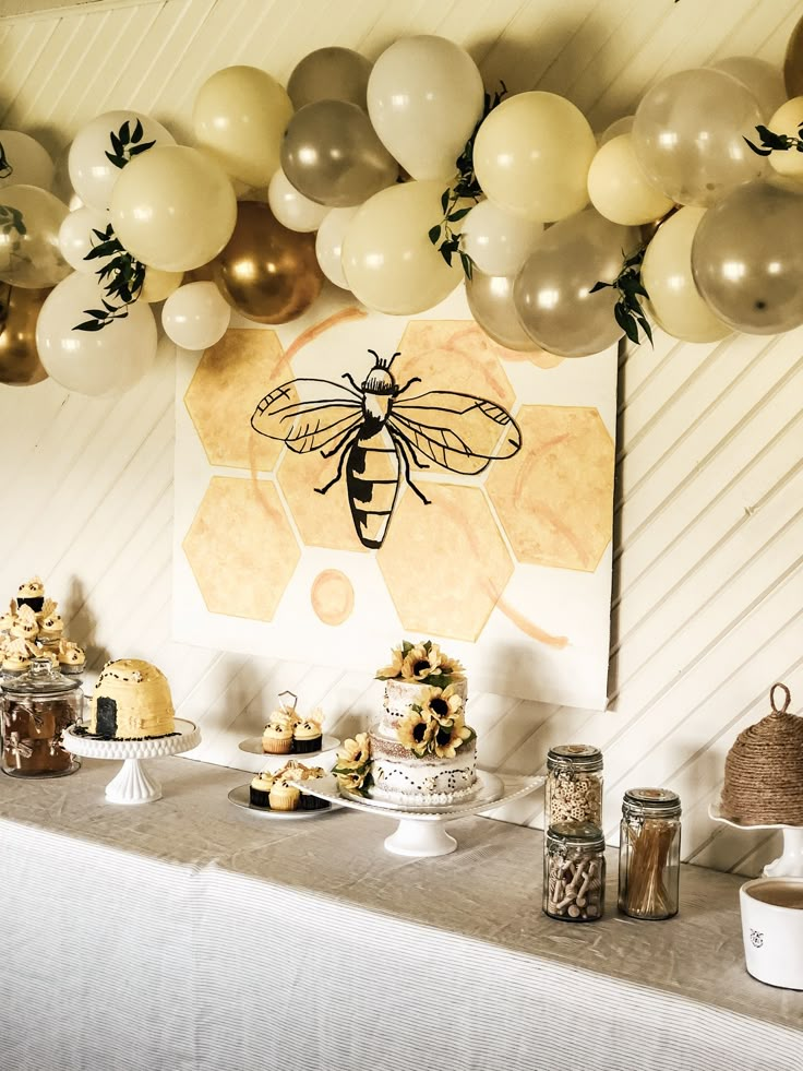 a table topped with cake and balloons next to a wall covered in honeycombs