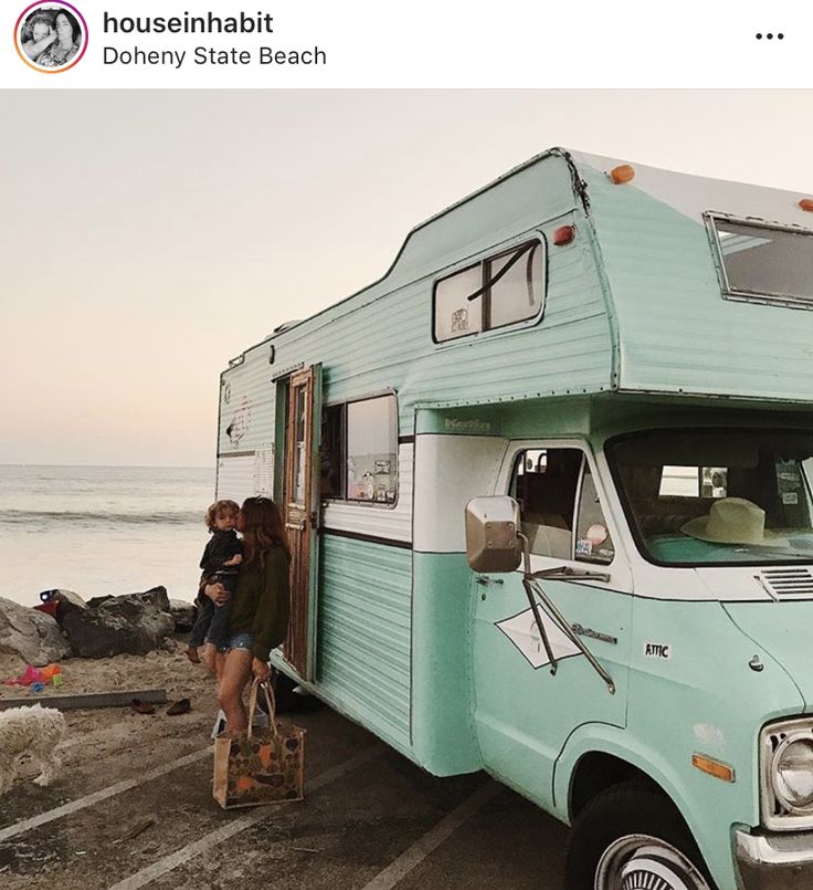 two people standing in front of an old camper on the beach near the ocean