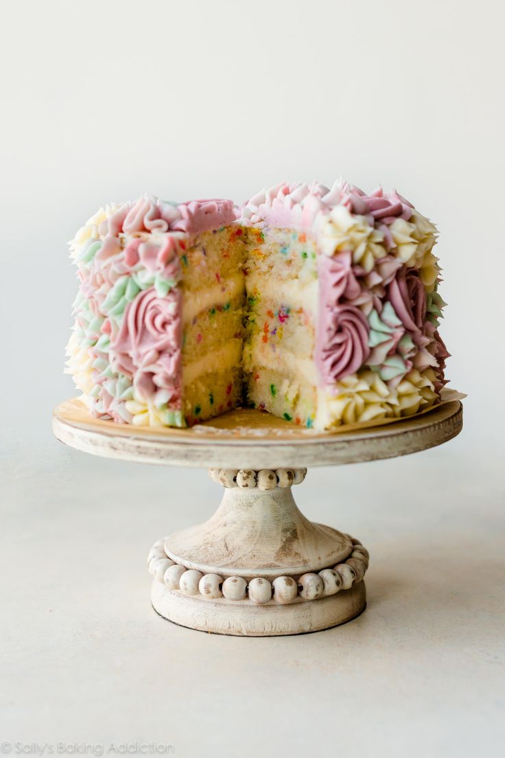 a white cake with pink frosting and sprinkles on top, sitting on a pedestal