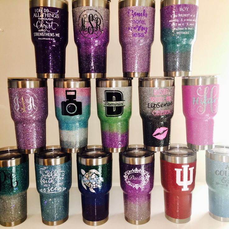 there are many different colored glitter tumblers on the table with each one's name