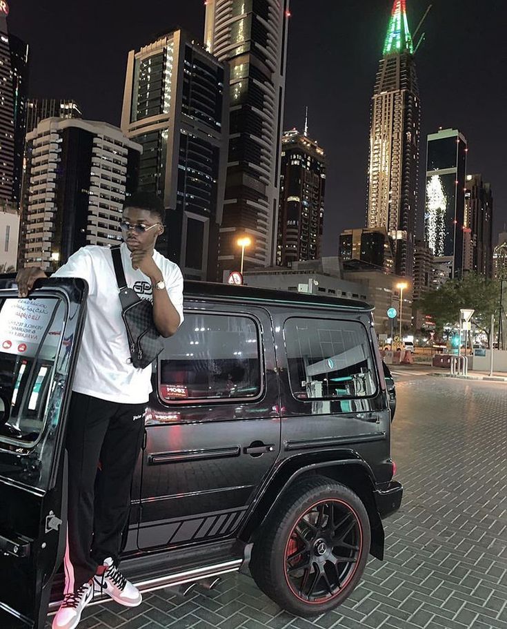 a man standing next to a black jeep in front of a cityscape at night