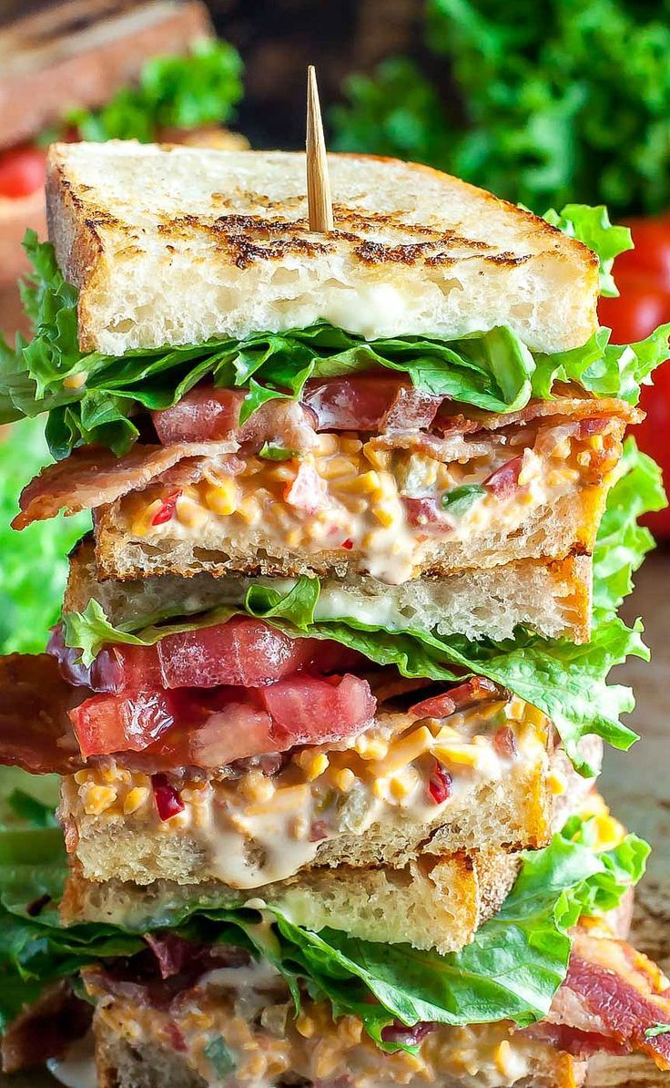 a bacon, lettuce and cheese sandwich stacked on top of each other with tomatoes in the background