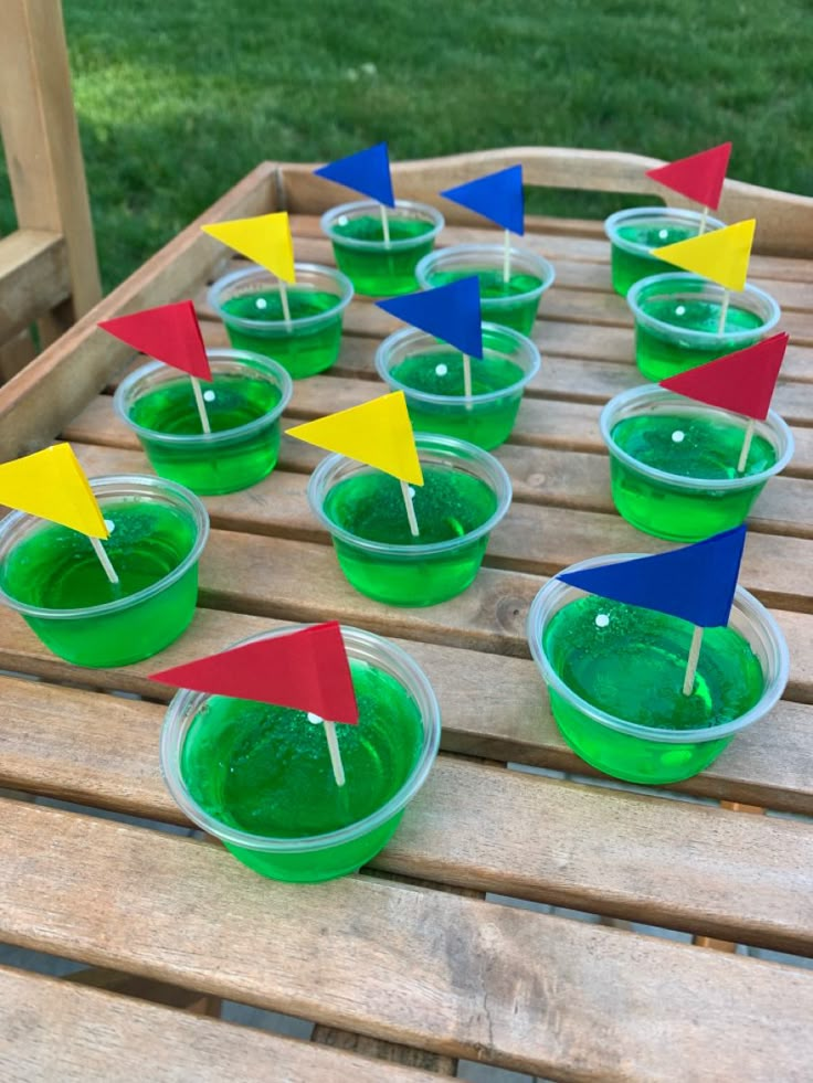 cups filled with green slime and red, yellow, and blue flags sitting on top of a wooden table