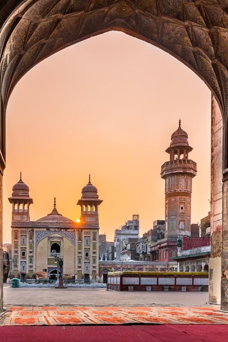 the sun is setting over an old city with tall buildings and arches in front of it