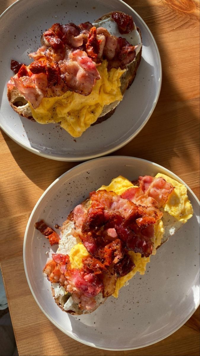 two white plates topped with breakfast foods on top of a wooden table next to each other