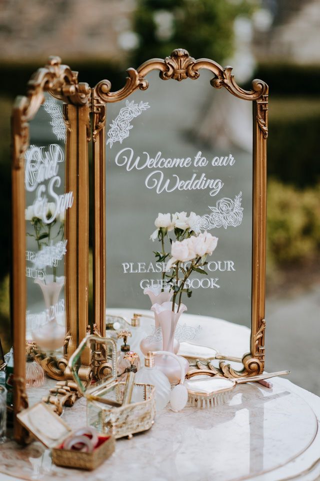 a wedding welcome sign and mirror on a table with flowers in vases next to it