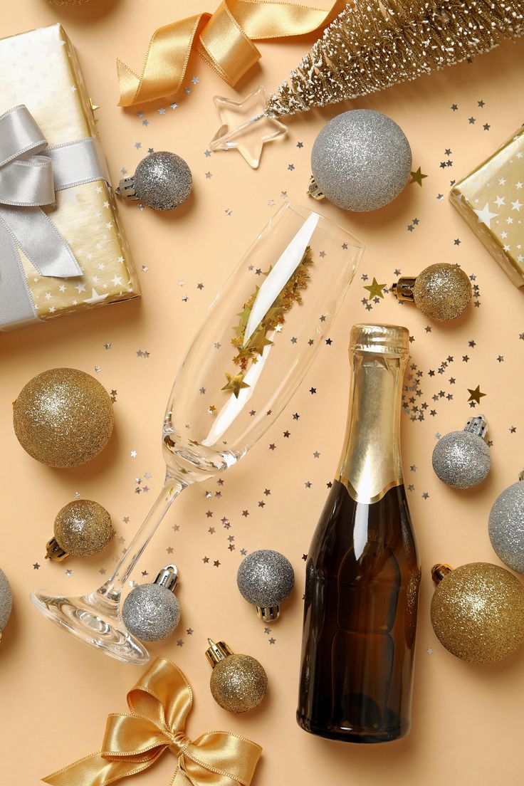 a bottle of champagne next to christmas ornaments and gifts on a table with gold ribbon