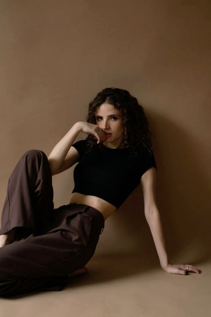 a woman sitting on the ground with her legs crossed and hands behind her head, wearing brown pants