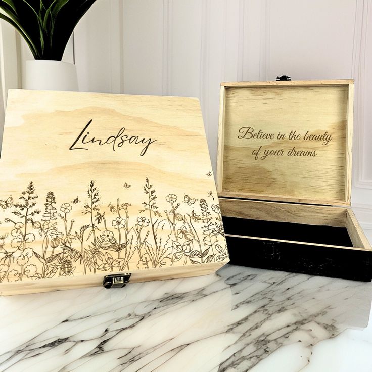 an open wooden box sitting on top of a marble counter next to a potted plant